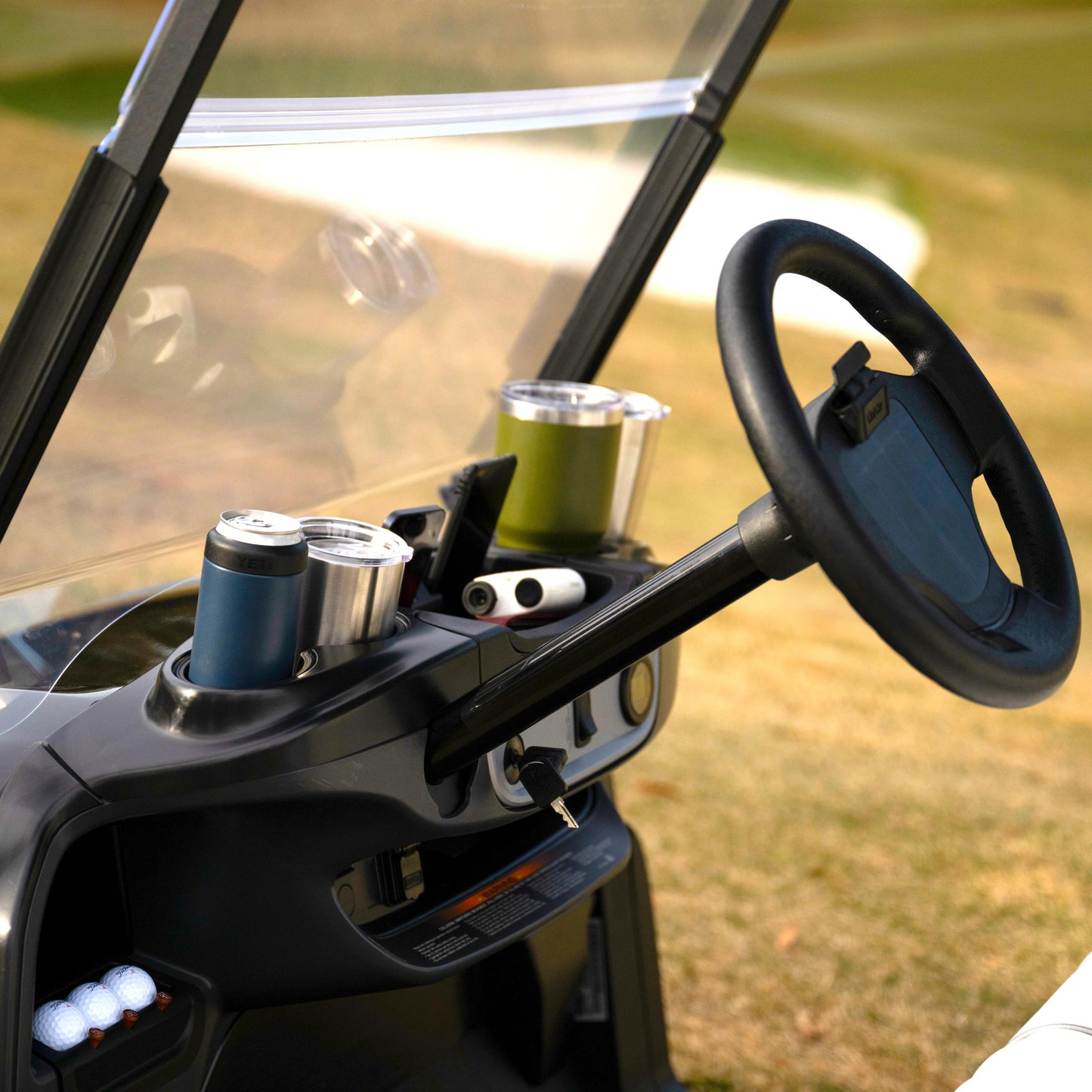 Club Car Golf cart interior with steering wheel, drinks and phone holder on a grassy background