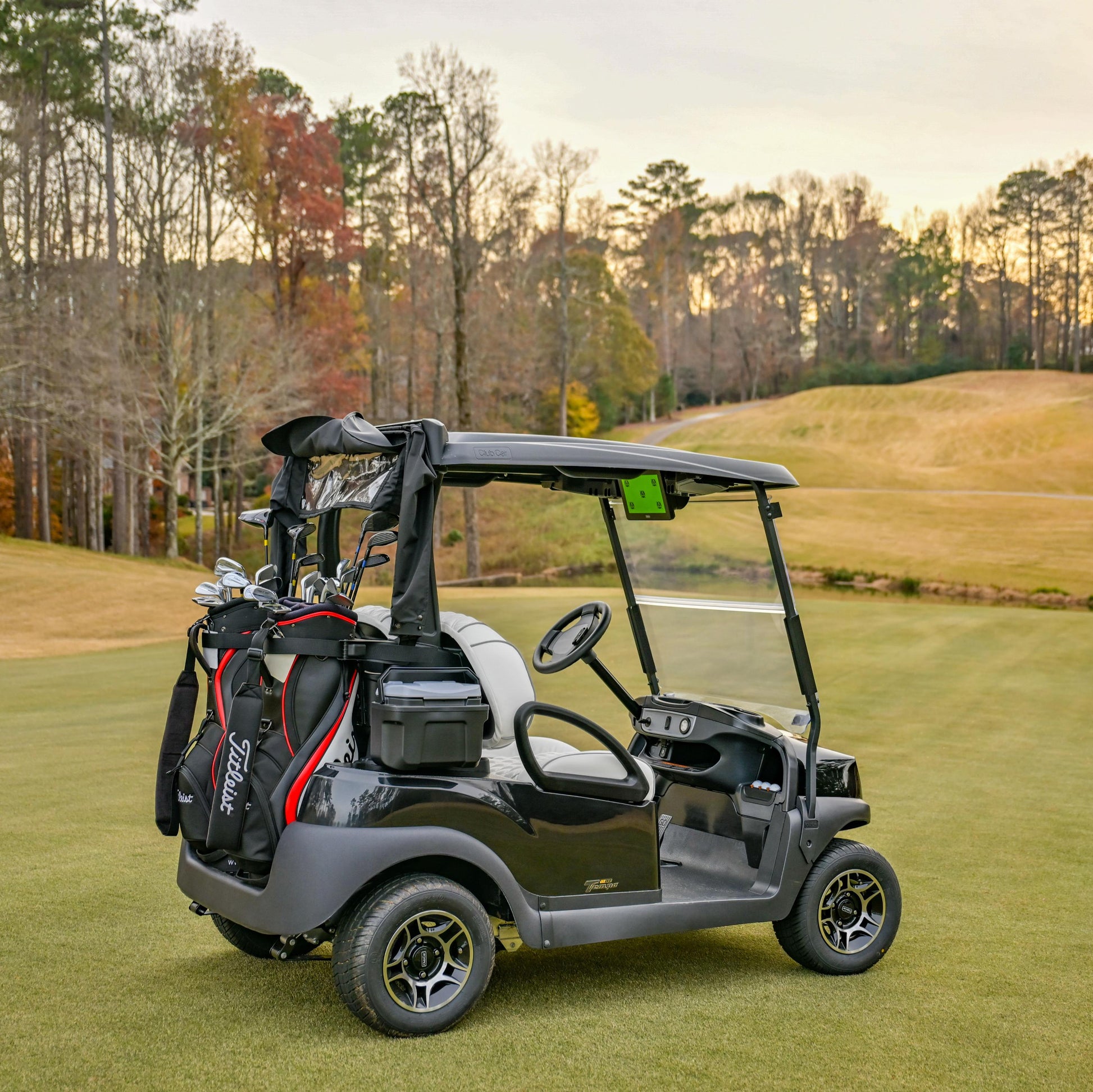 Black Club Car Tempo Golf cart on a golf course with trees and sunset in the background